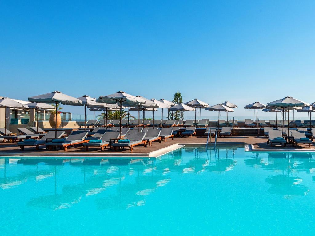 Peldbaseins ar sauļošanās krēsliem un parasoliem, kas izvietoti pie ūdens, skaidrā zilā debesīs. Ideāla vieta relaksācijai un atpūtai.