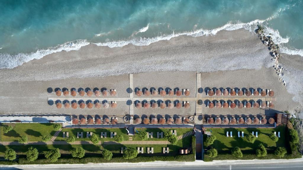 Pludmales ainava ar saulessargiem un sauļošanās krēsliem, kas sakārtoti uz smilšainas pludmales, blakus mierīgai jūras viļņu līnijai.