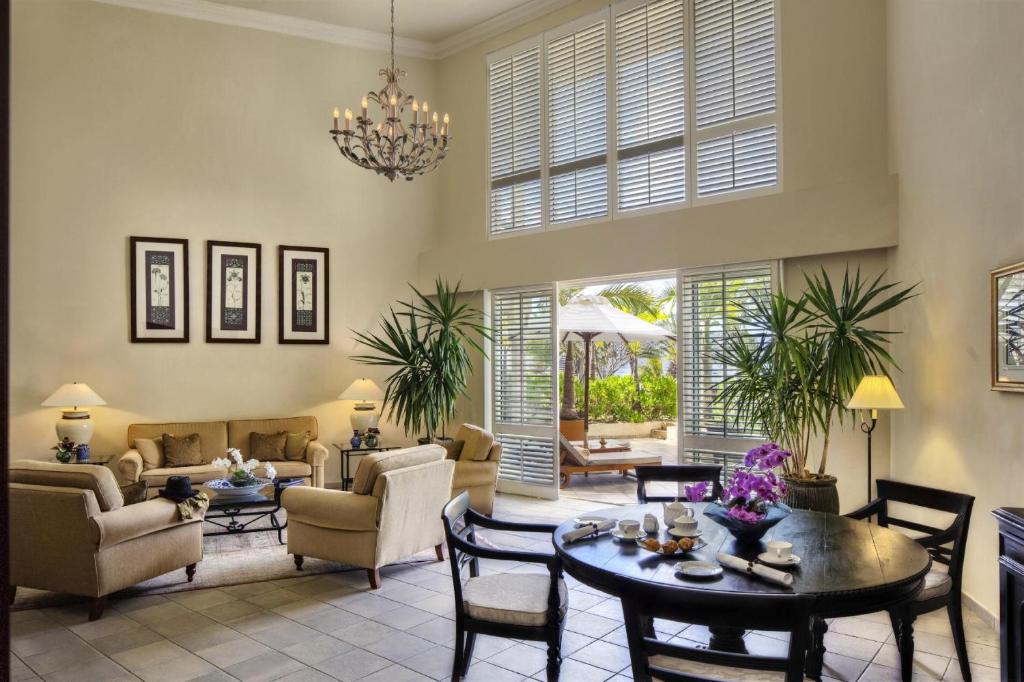 Mūsdienīgs viesistabas interjers ar augstiem griestiem, ērtām mēbelēm un plašiem logiem, caur kuriem redzams dārzs. Telpā ir dabiski apgaismojums un eleganta dekorācija.