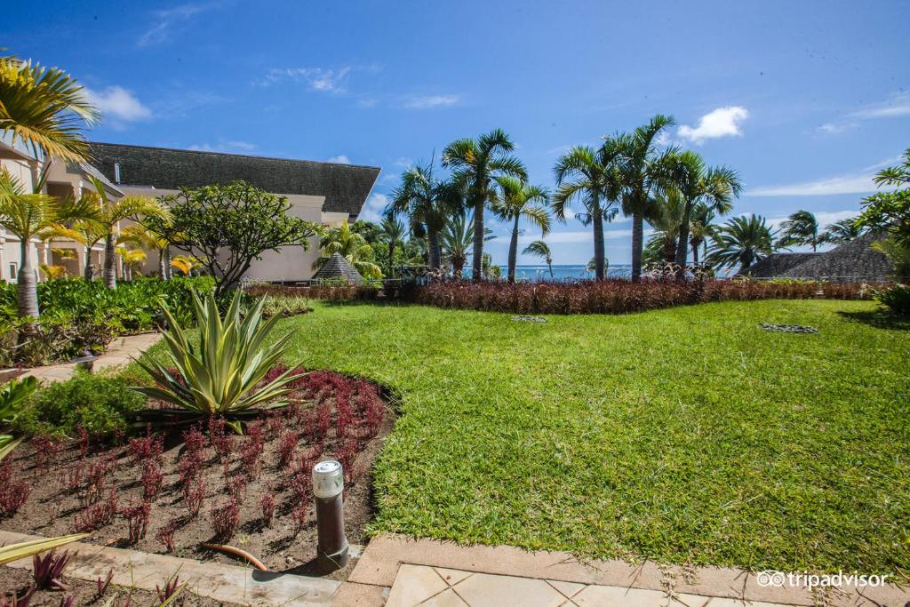 Skaists tropu dārzs ar zālienu un palmām, kas sniedzas līdz jūrai, radot mierīgu un relaksējošu atmosfēru. Ideāla vieta atpūtai un dabas baudīšanai.