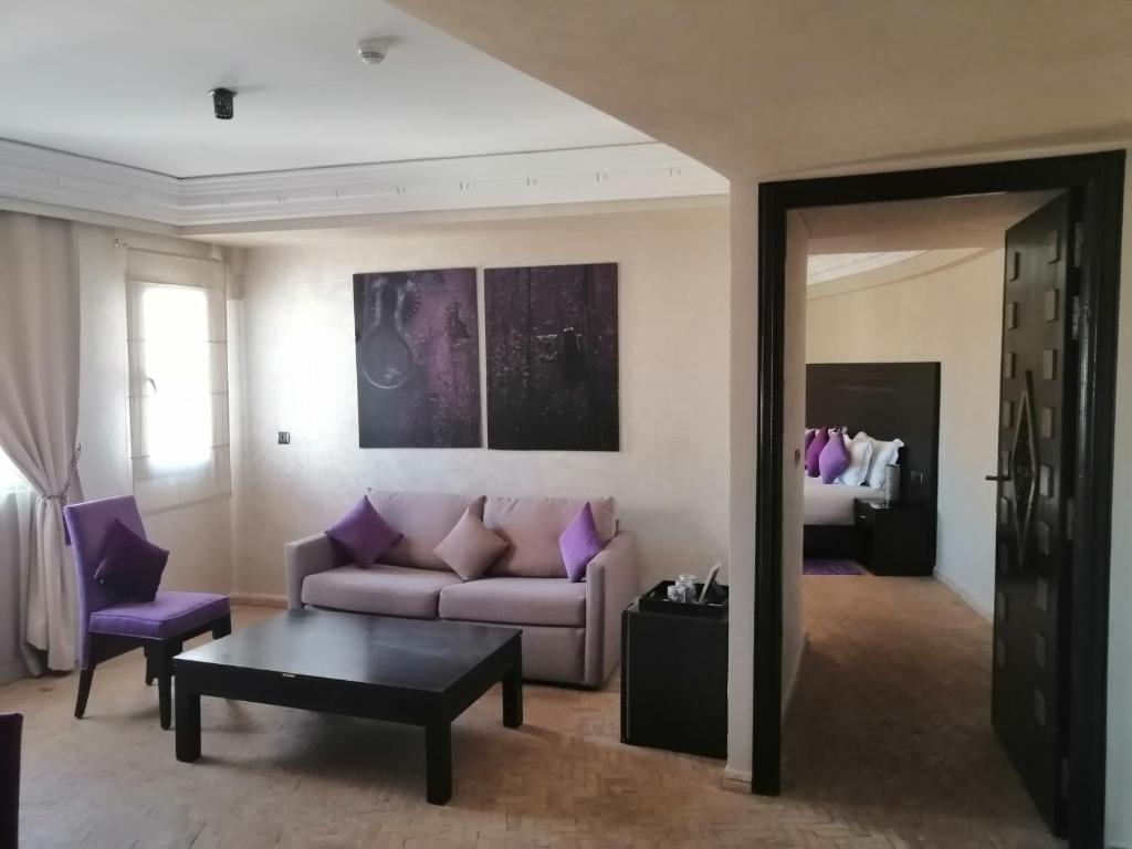 Mūsdienīgs viesnīcas numurs ar ērtu dīvānu un krēsliem purpursarkanā krāsā, melna galda un mākslas darbiem uz sienas. Telpa piedāvā gaišus logus un pieeju uz guļamistabu.