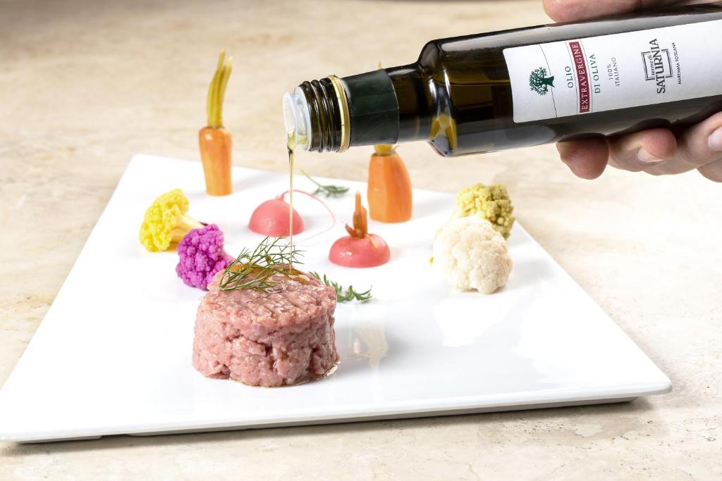 Kvalitatīvas olīveļļas lej uz gourmet šķīvja ar liellopa tartaru un krāsainiem dārzeņiem.