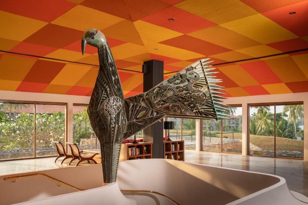 Mūsdienīga interjera dizaina telpa ar krāsainu griestu apdari un lielu, izsmalcinātu putna skulptūru centrā. Gaisma ieplūst caur lielajām logu sienām, radot atvērtu un gaisīgu atmosfēru.