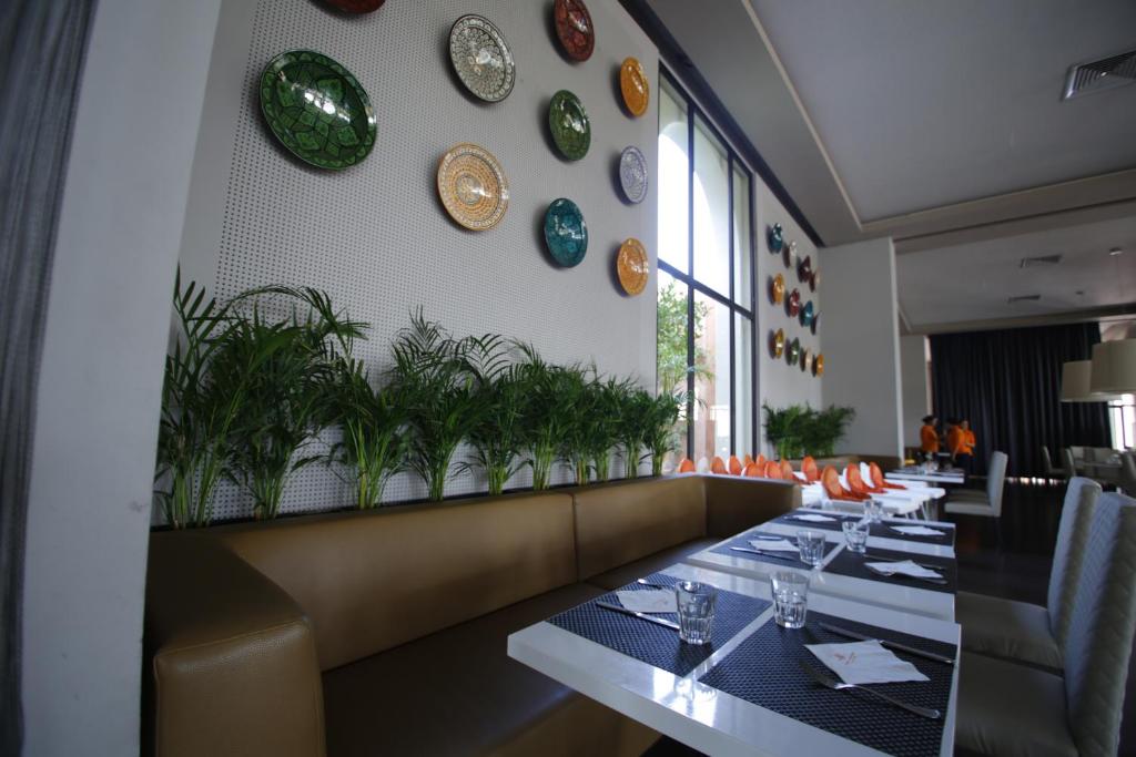 Moderns restorāns ar dekoratīvām šķīvju kolekcijām uz sienas un zaļiem augiem. Gaisīga atmosfēra un elegants interjers, kas nodrošina patīkamu ēdināšanas pieredzi.