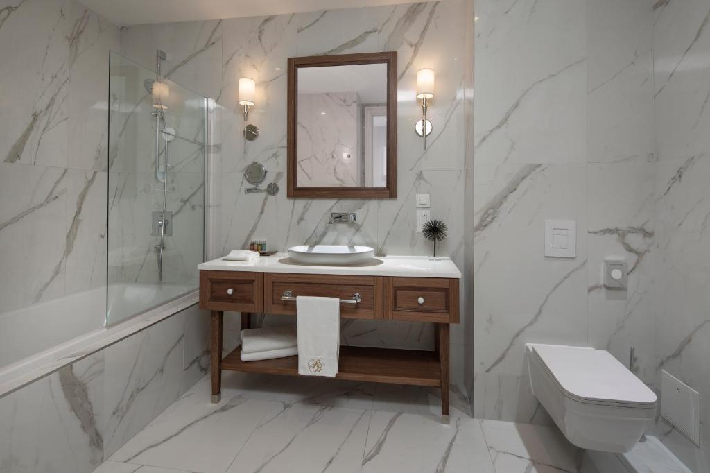 Mūsdienīgs vannas istabas interjers ar marmora sienām, koka izlietni un elegantu apgaismojumu. Stilīgā dizaina elementi rada patīkamu un relaksējošu atmosfēru.