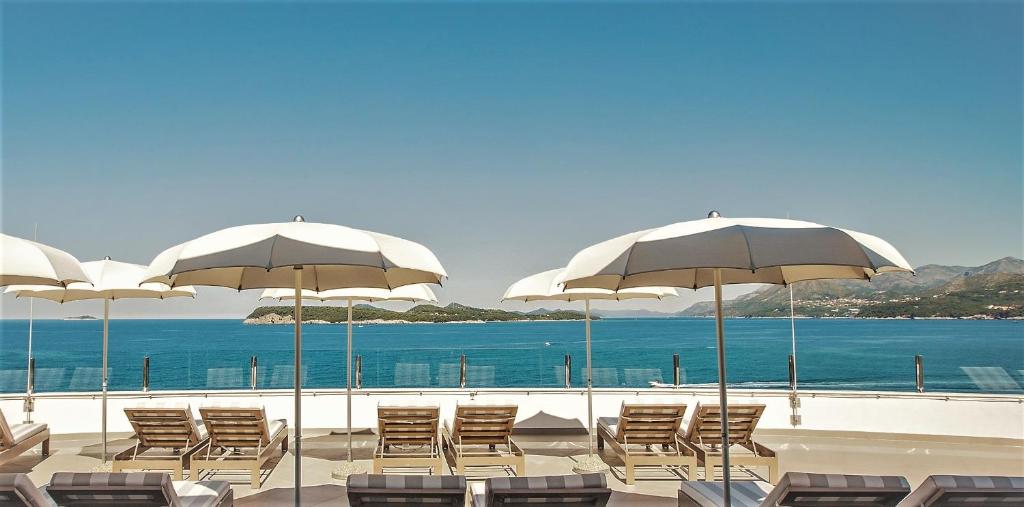 Saulainā terase ar sauļošanās krēsliem un baltajiem lietussargiem, kurā redzama gleznaina jūra un kalnu ainava. Ideāla vieta atpūtai un relaksācijai.