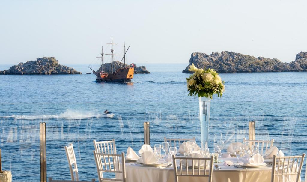 Romantisks skats uz jūru ar svinību galdu priekšplānā, kamēr tālumā redzama kuģis un klintis.