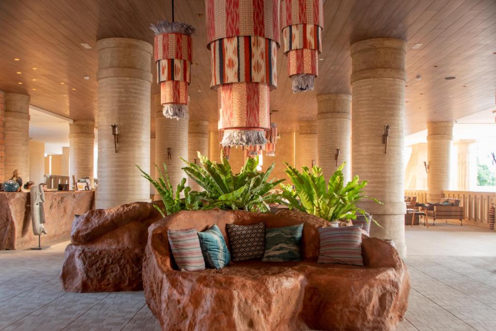 Mūsdienīgs viesnīcas interjers ar akmens dīvānu, spilveniem un dekoratīvām lampām, kas rada siltu un uzaicinošu atmosfēru. Zaļās augu kompozīcijas papildina telpas estētiku.