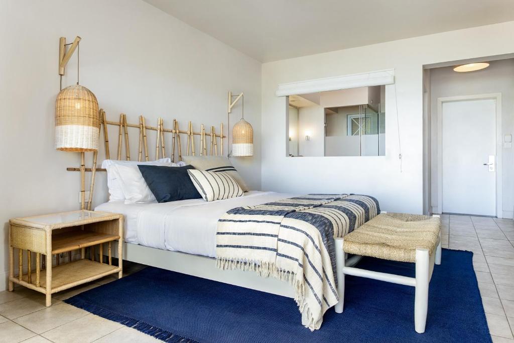 Mūsdienīgs guļamistabas interjers ar gultu, dabīgas krāsas dekoriem un bāra gaismas ķermeņiem. Telpa ir gaiša un plaša, ar modernām mēbelēm un paklāju.