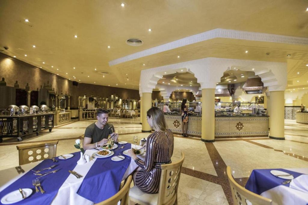 Svaigā un eleganta restorāna iekārtojums ar apgaismojumu, kur pāris bauda maltīti pie galda, bet citi viesi izvēlas ēdienus no bufetes.