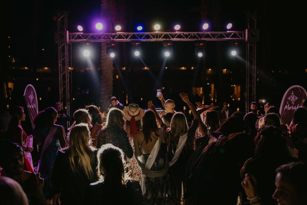 Viesi izbauda nakts pasākumu Meraki Resort piekrastē ar skatu uz skatuves gaismām.