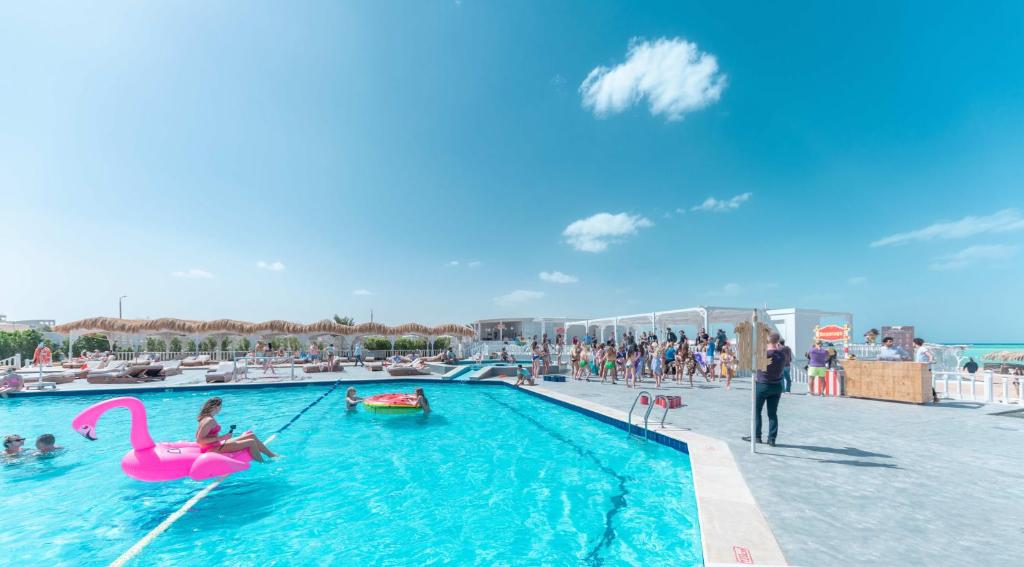 Viesnīcas Meraki Resort baseins ar cilvēkiem un rozā pīli.