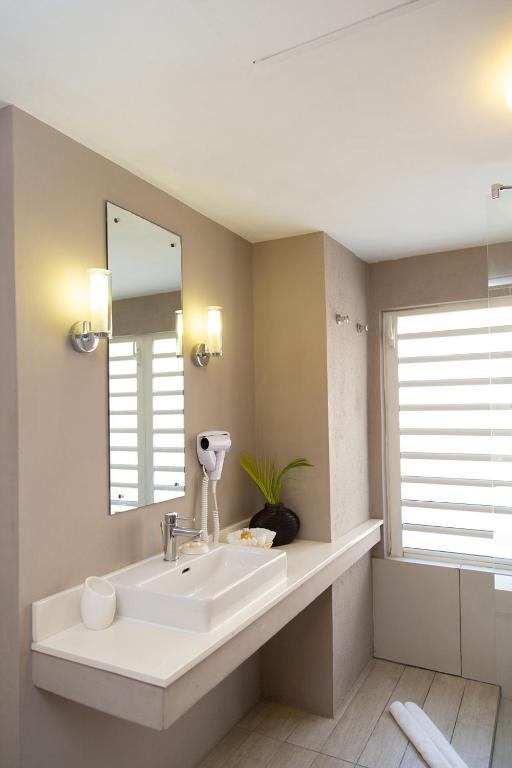 Mūsdienīgs vannas istabas interjers ar plašu izlietni, spoguli un higiēnas piederumiem. Gaisma rada patīkamu atmosfēru, un logs nodrošina dabīgu apgaismojumu.