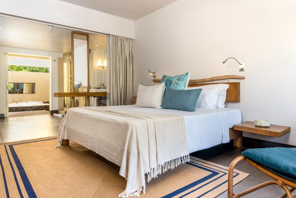 Mūsdienīgs guļamistabas interjers ar gultu un dekoratīviem spilveniem, kas rada mierīgu atmosfēru. Telpā ir redzams atvērts plāns, kas savieno vannas istabu ar guļamistabu.