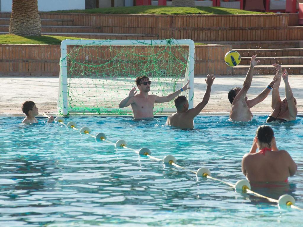 Ūdenspolo spēle baseinā, kur dalībnieki aktīvi piedalās, mēģinot gūt vārtus. Šķiet, ka ir jautrs un dinamiskas atmosfēras brīdis.