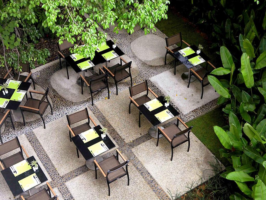 Ārtērijas terase ar melnām galdiem un zaļiem ēdienkartes lapām, ko ieskauj zaļumi un augi. Klusa un relaksējoša atmosfēra, ideāla maltītei ārā.