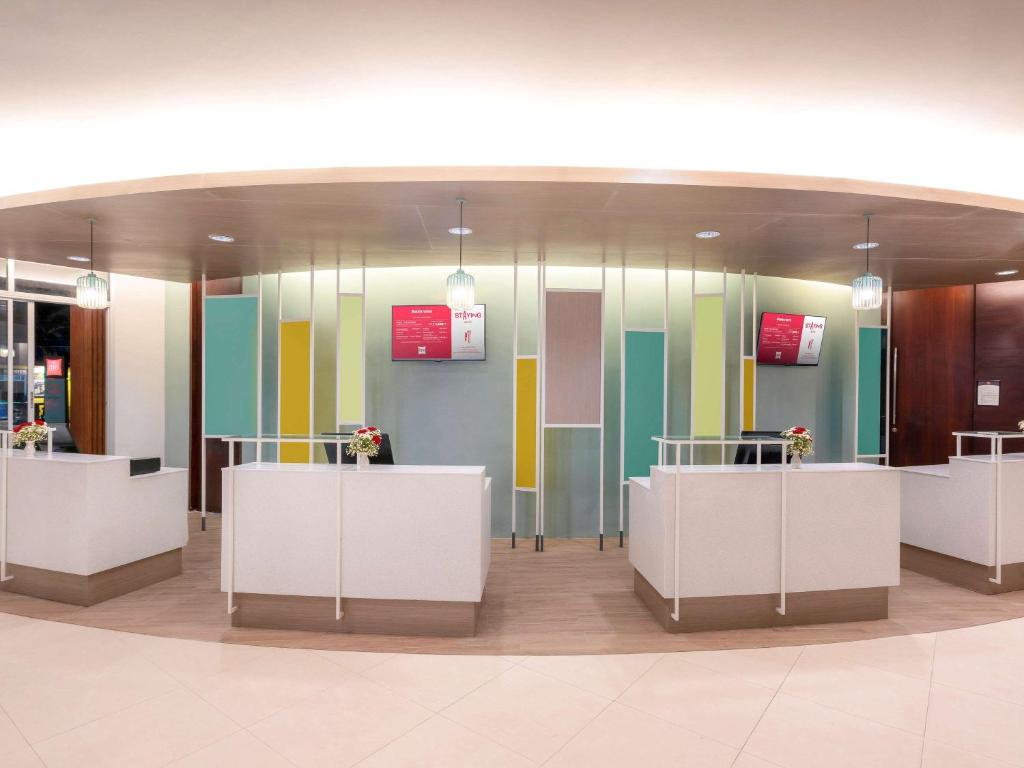 Mūsdienīgs reģistratūras interjers ar gaišām krāsām un ziedu kompozīcijām uz galdiem. Attēlā redzami reģistratūras galdi, kas izkārtoti pārdomāti, ar stilīgu apgaismojumu un informatīvām plāksnēm.