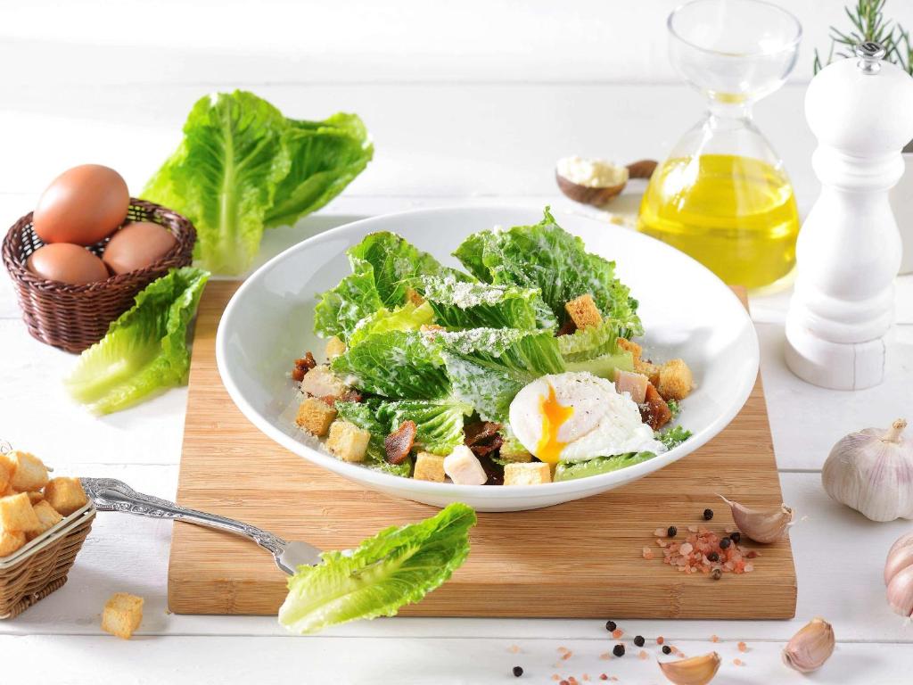 Svaigu salātu bļoda ar romiešu salātiem, grauzdiņiem un vārītu olu, papildināta ar olīveļļu un ķiplokiem. Fons ar olu un garšvielām.
