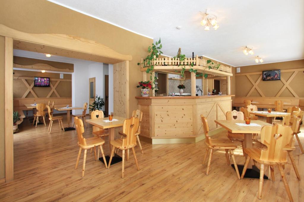 Restorāna interjers ar koka mēbelēm un siltu apgaismojumu, kas rada mājīgu atmosfēru. Redzamas ēdamgaldi un bāra zona ar augiem un dekorācijām.