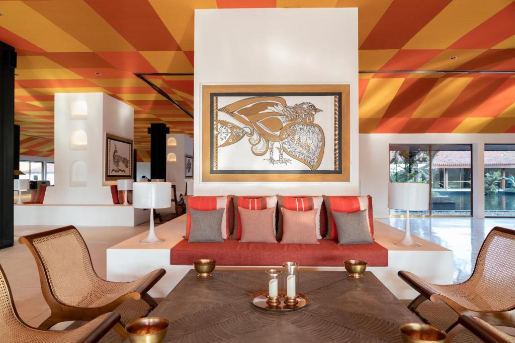 Mūsdienīgs viesnīcas interjers ar spilgtu dzeltenu un oranžu griestu dizainu, sarkanām un pelēkām spilvenām uz dīvāna, kā arī mākslas darbu uz sienas. Eleganti mēbeļu elementi un gaismas piešķir telpai siltumu un viesmīlību.