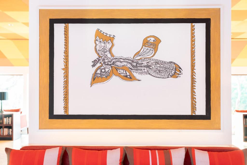 Sienas gleznojums ar oranžiem un melniem akcentiem, attēlojot stilizētu putnu vai tauriņu. Fons ir balts, un glezna ir ietverta zeltainā apmalē.