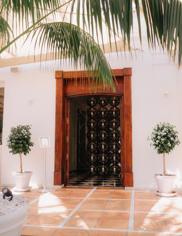 Eleganta ieeja ar koka durvīm un melnu rotājumu, ko ieskauj zaļas augu kompozīcijas un flīžu grīda.