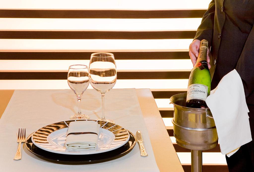 Galda klājums ar vīna glāzēm un šampanieša pudeli, ko pasniedz eleganti. Uz galda redzama melna un balta trauku kombinācija.