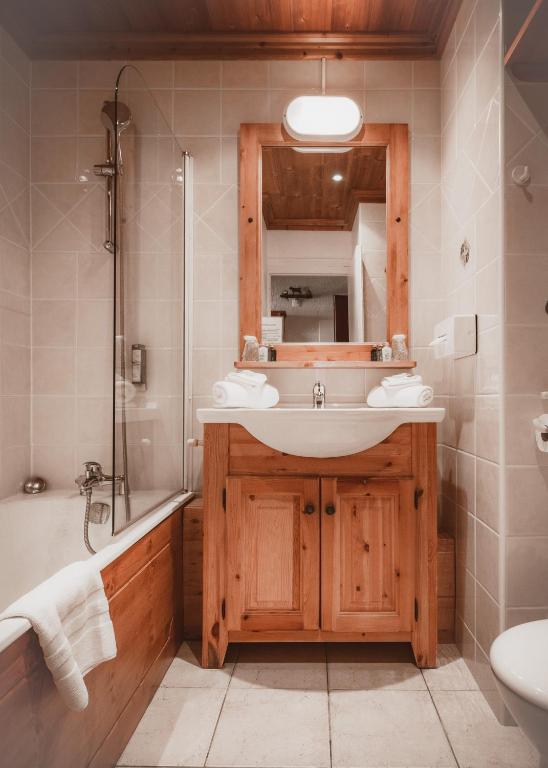 Mūsdienīgs vannas istabas interjers ar koka elementiem, iekļaujot dušu un vannu. Vannas istabā ir liels spogulis un elegants izlietnes skapis.