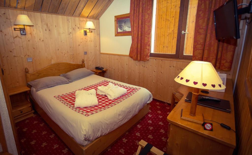 Mūsdienīga viesnīcas istaba ar koka apdari, divguļamo gultu un siltu apgaismojumu. Istabā ir logi ar aizkariem un televizors uz galda.