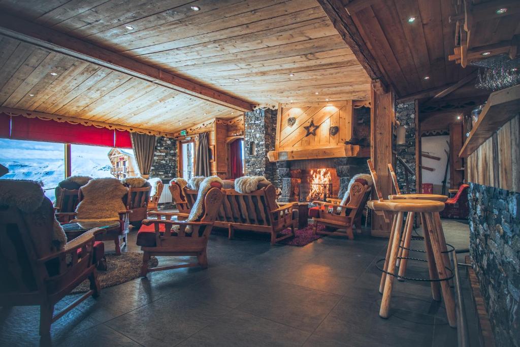 Mūsdienīga kalnu mājas viesistaba ar koka apdari, ērtām krēslām un kamīnu, kas rada siltu un mājīgu atmosfēru. Lielie logi piedāvā skatu uz sniegotām ainavām.