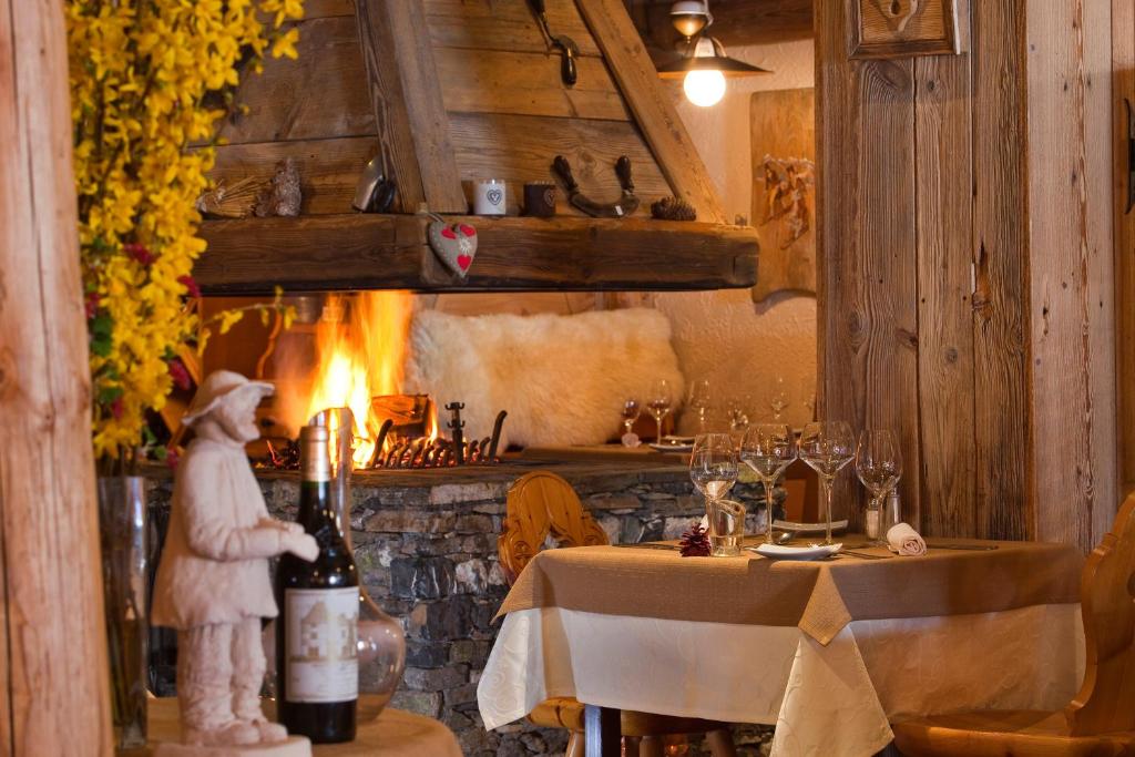 Mājīga ēdamzāle ar akmens kamīnu un sveču gaismu. Uz galda ir vīna pudele un eleganti glāzes, radot siltu atmosfēru.