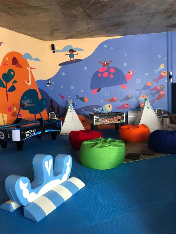 Bērnu spēļu telpa ar krāsainu sienu gleznojumu, spēļu galdu un spilveniem. Ideāli piemērota rotaļām un izklaidei.
