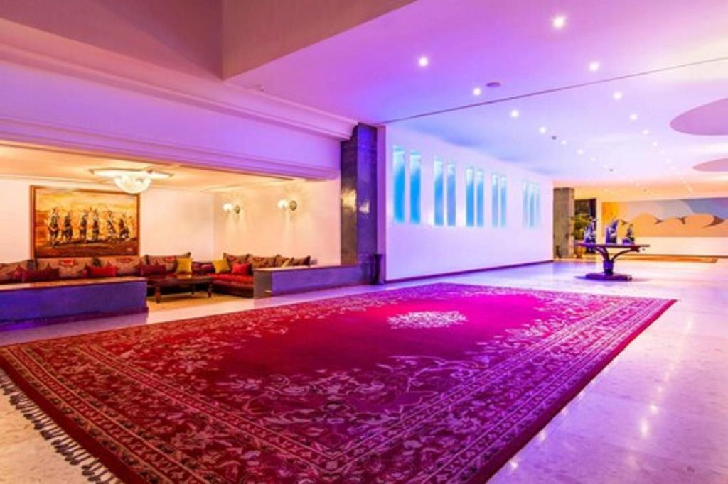 Luksusa viesnīcas vestibils ar sarkanu paklāju, komfortablām mēbelēm un mūsdienīgu apgaismojumu. Sienas rotā mākslas darbi, radot elegantu atmosfēru.