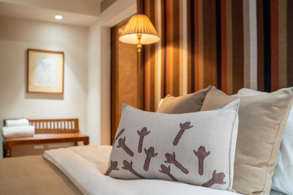 Gultas spilvens ar interesantu dizainu, kas izceļas uz fonā esošā strīpainā sienas apdares. Mierīga guļamistabas atmosfēra ar gaismas avotu un koka mēbelēm.