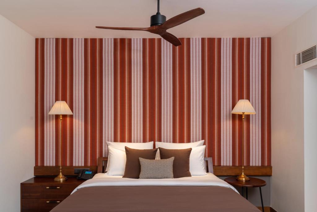 Mūsdienīga guļamistaba ar siltu krāsu paleti, svītrainu sienu un elegantiem gaismekļiem abās pusēs. Gultā ir ērti spilveni un gultas veļa, radot relaksējošu atmosfēru.