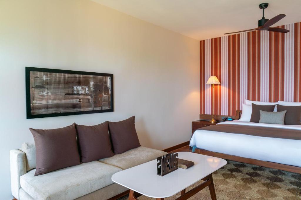 Mūsdienīgs viesnīcas numurs ar komfortablu dīvānu, dekoratīviem spilveniem un modernu gultu. Sienas rotā krāsaini svītraini tapetes, radot siltu un viesmīlīgu atmosfēru.