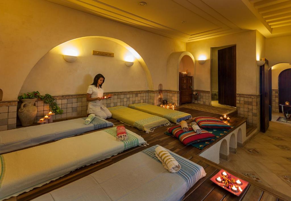 Relaksējoša spa telpa ar masāžas gultām, svecēm un augu dekorācijām, kurā profesionāla masiere sagatavo jautājumus klientu labsajūtai.