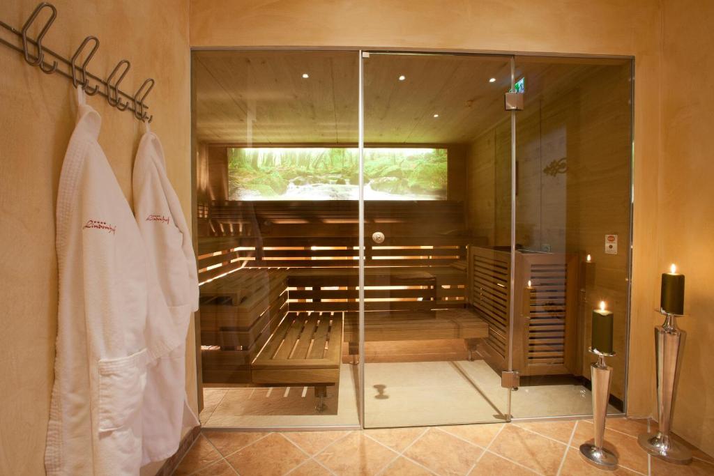 Mūsdienīga sauna ar stikla durvīm, kurā redzami koka sēdekļi un relaksējoša dabas ainava uz ekrāna. Blakus karstas sveces un baltas peldmēteļi.