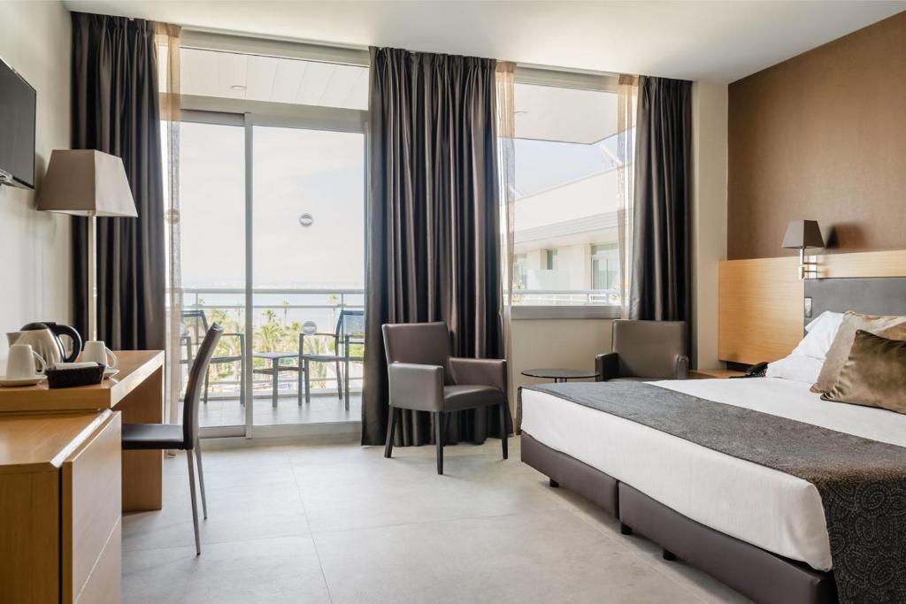 Mūsdienīga viesnīcas numura iekšskats ar ērtu gultu, darba galdu un balkonu, no kura paveras skats uz dārzu un jūru. Interjers ir stilīgs un gaišs, radot patīkamu atmosfēru.