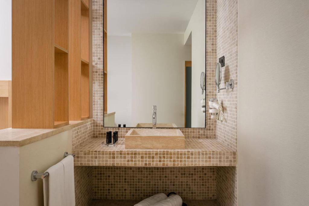 Mūsdienīgs vannas istabas interjers ar mozaīkas flīzēm, elegantu spoguli un akmens izlietni. Interjers ir gaišs un minimālistisks, piedāvājot stilīgu un funkcionālu telpu.