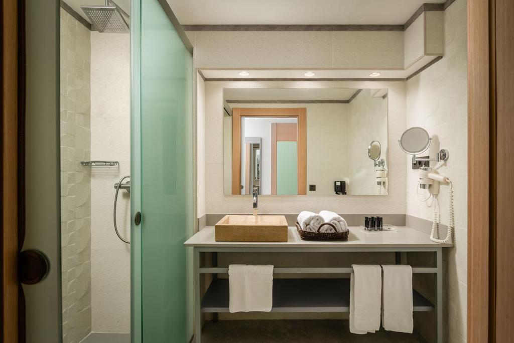 Moderns vannas istabas interjers ar dušu, spoguli un tīru, organizētu darba virsmu. Zvanveida dvieļi un higiēnas piederumi pieejami uz galda.