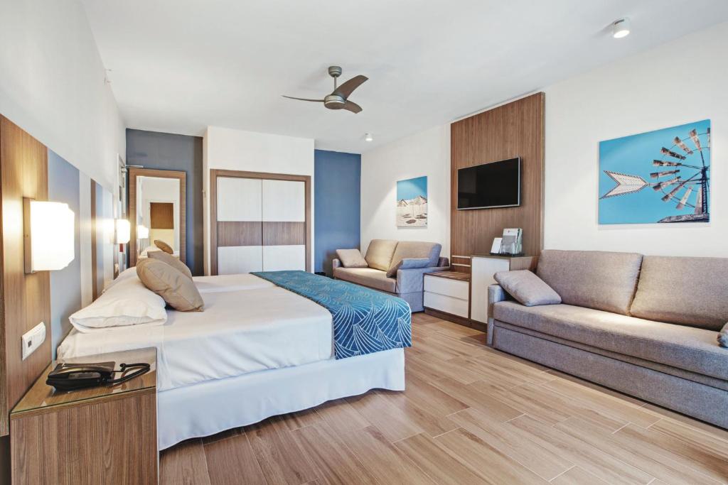 Mūsdienīgs viesnīcas numurs ar divguļamo gultu, dīvānu un televizoru. Telpas interjers ir gaišs un elegant, ar koka grīdām un dekoratīvām gleznām uz sienām.