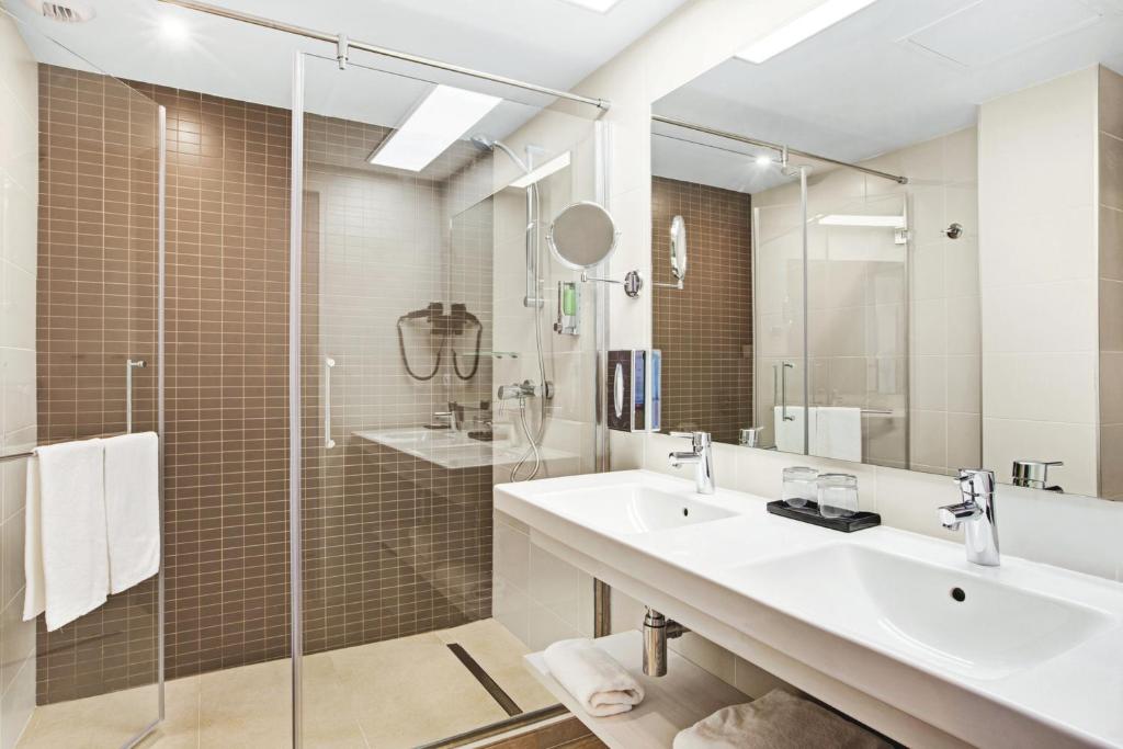 Mūsdienīgs vannas istabas interjers ar stikla dušu un divām izlietnēm, kas piedāvā elegantu dizainu un funkcionālumu.