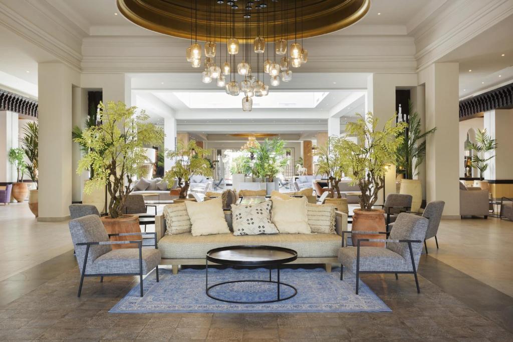 Mūsdienīgs viesnīcas vestibilis ar elegantu interjeru, mājīgu dīvānu, stilīgām krēslām un zaļām augiem, kas rada relaksējošu atmosfēru. Gaismas ķermeņi piešķir telpai siltumu un viesmīlību.