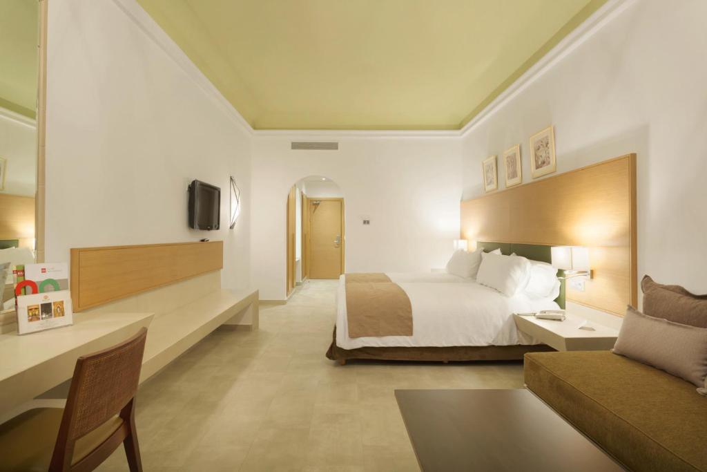 Mūsdienīgs viesnīcas numurs ar divām gultām, dīvānu un rakstāmgaldu. Telpa ir gaiša un plaša, ar neitrālām krāsām un modernām mēbelēm.