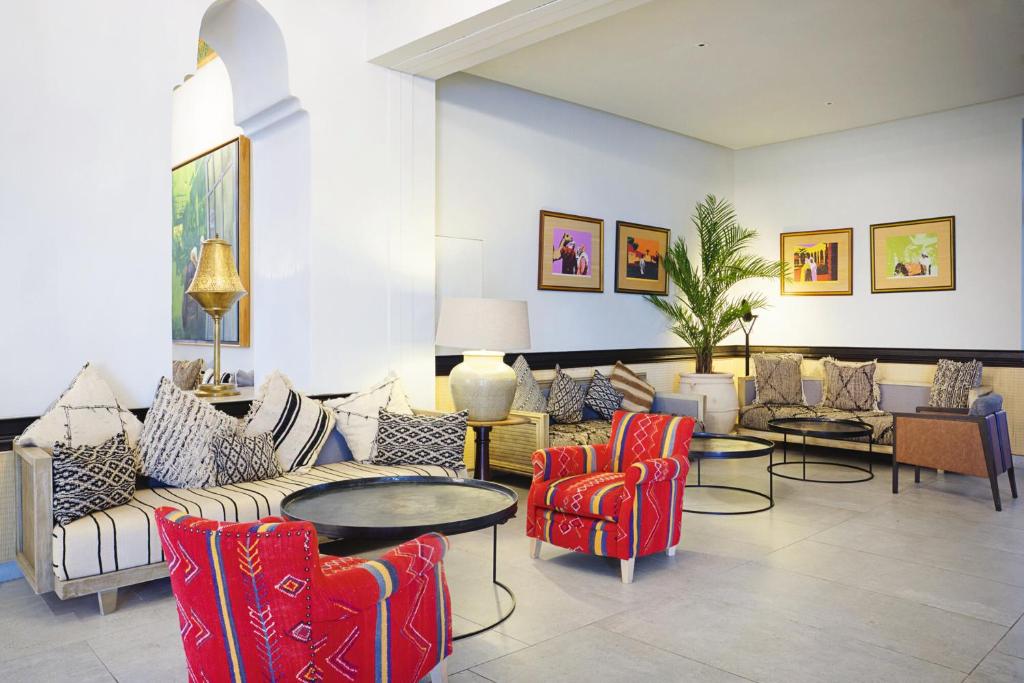 Mūsdienīgs viesnīcas uzņemšanas laukums ar ērtām dīvānu grupām, spilveniem un krāsainām krēslām, kas rada viesmīlīgu atmosfēru. Sienas rotā krāsaini mākslas darbi, pievienojot interjeram dzīvīgumu.