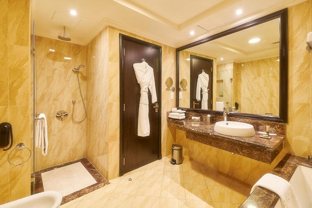 Moderns vannas istabas interjers ar zeltainu flīžu apdari, dušu un elegantu spoguli. Izcila higiēnas telpa ar mūsdienīgām iekārtām un komfortu.