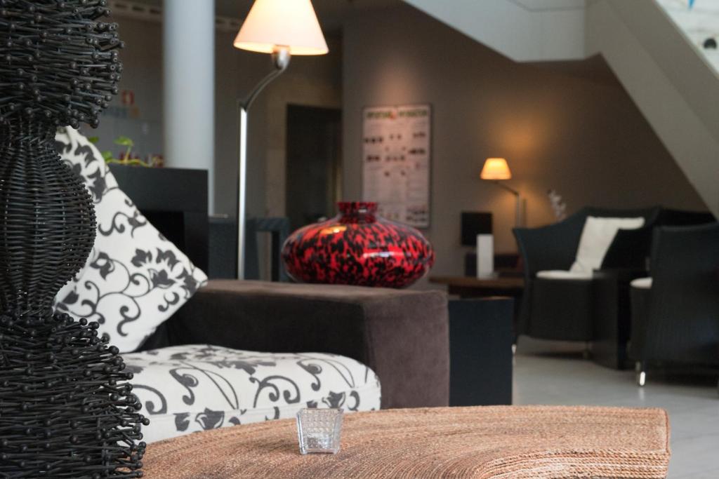 Mūsdienīgs viesnīcas interjers ar melnu un baltu rakstainu dīvānu, sarkanu vāzi un elegantu apgaismojumu. Rūpīgi izstrādāta telpa, kas aicina uz relaksāciju.