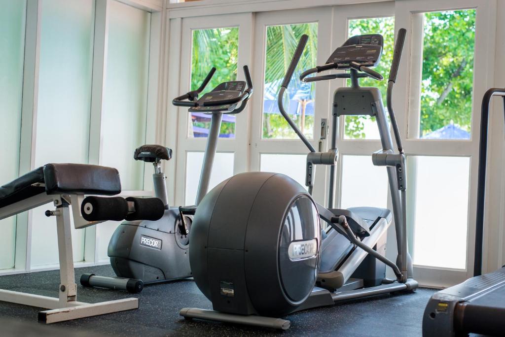 Sporta zāle ar dažādiem trenažieriem, tostarp eliptiskais trenažieris un velosipēds, kas izvietoti gaišā telpā ar lieliem logiem.