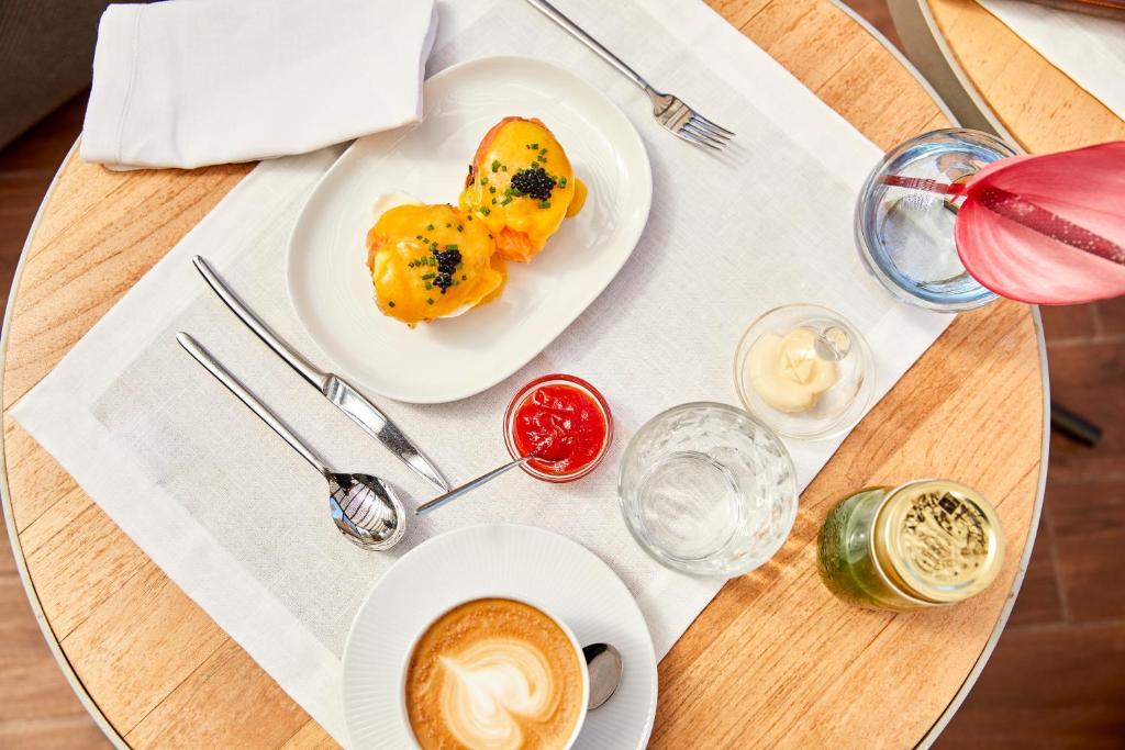 Broka ar izsmalcinātu ēdienu un dzērieniem, tostarp olu benedikta, kafiju un desertiem, uz koka galda.